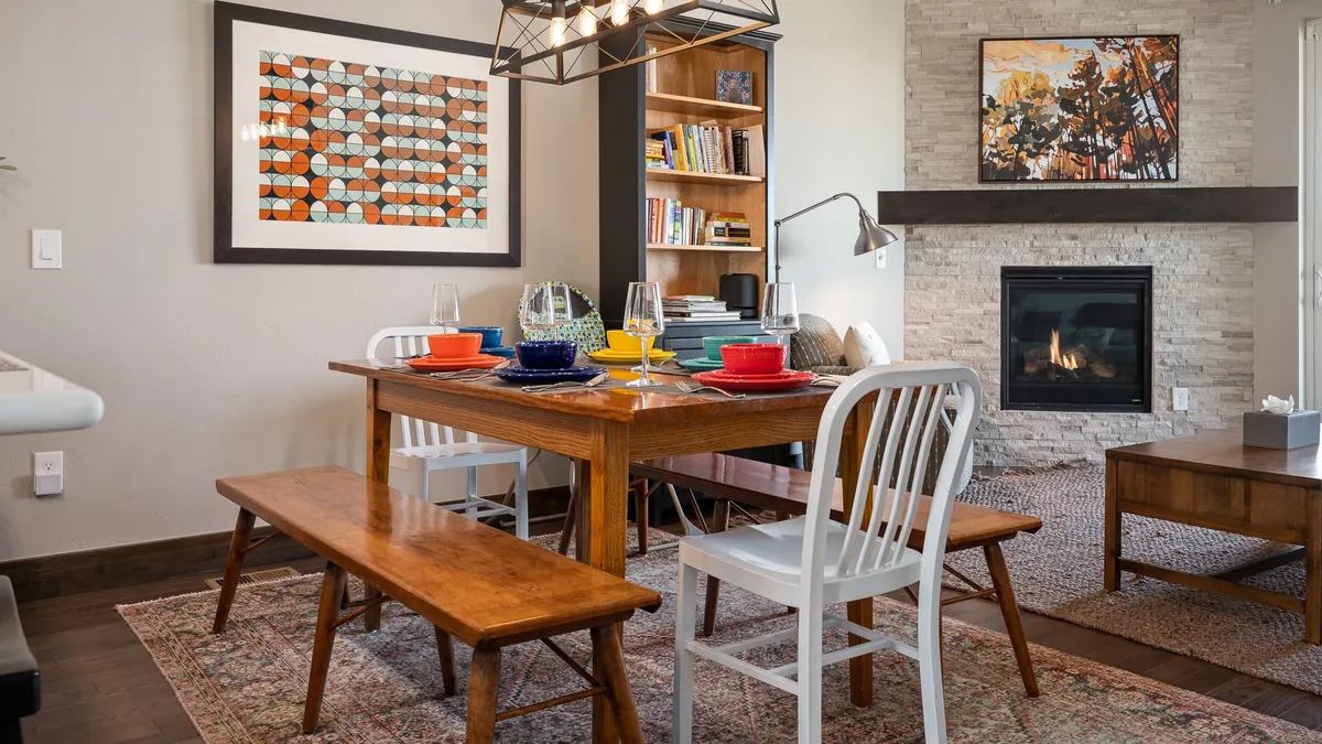 A cozy interior space showcasing a dining table set for eight, positioned near a contemporary fireplace with artwork above. The setting is intimate and welcoming, encouraging shared meals, laughter, and memorable evenings.
