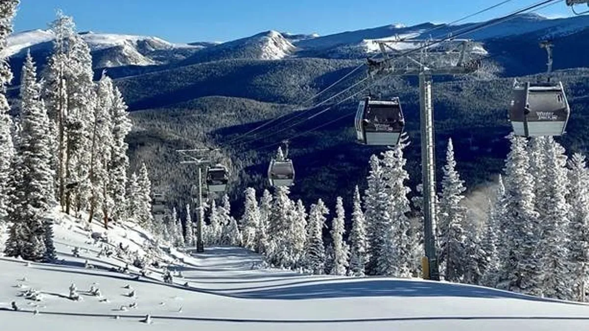 This image captures a serene and adventurous winter landscape with ski gondolas moving over snow-covered trees and a dramatic mountain backdrop. The scene evokes both the thrill of winter sports and the natural beauty of the surroundings.