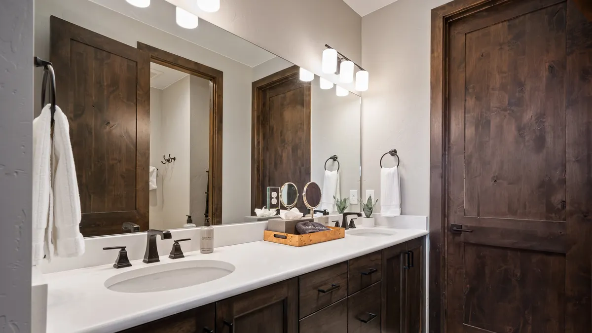 A modern bathroom with double sinks, sleek wooden cabinetry, and decorative accents. Sunlight streams in, creating an atmosphere of calm and self-care.