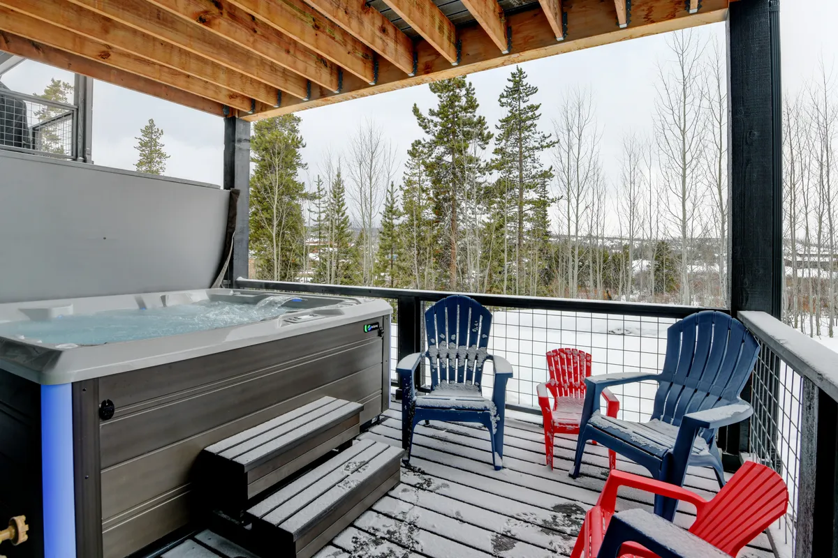 An inviting exterior space featuring a hot tub surrounded by adirondack chairs and a snowy landscape. The setting is cozy and private, perfect for family relaxation after indoor play.
