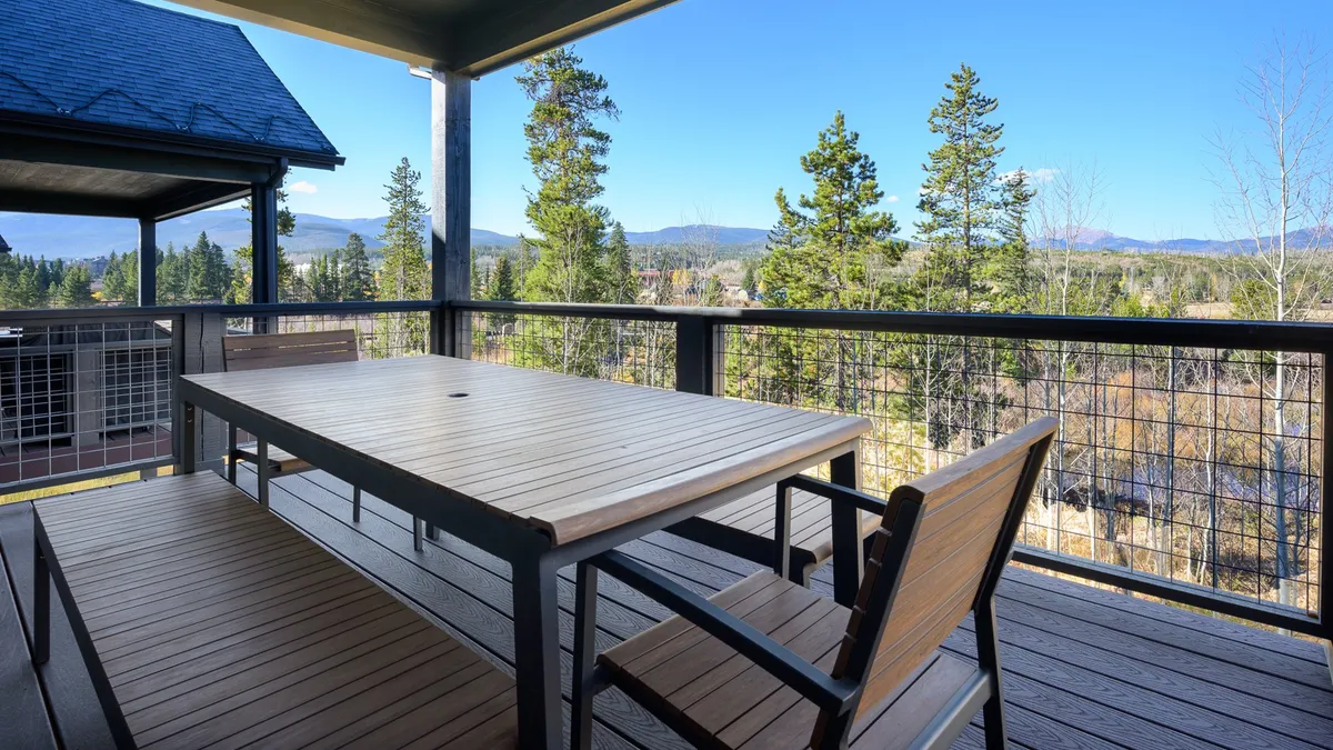 An upper deck with a dining table and chairs overlooks a stunning mountain view, with Byers Peak visible on the horizon and trees providing a sense of privacy. The scene invites guests to enjoy morning coffee or evening gatherings while appreciating the Rocky Mountain panorama.