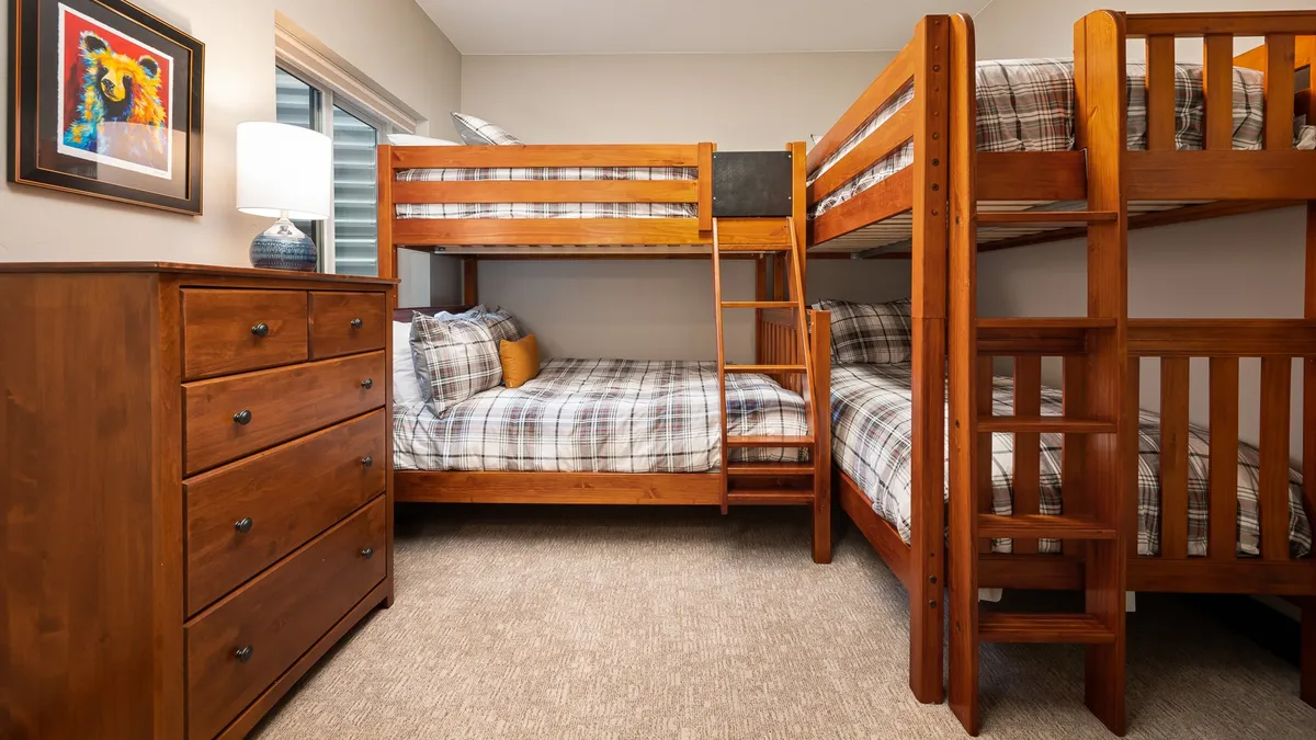 This image shows a cozy bedroom with inviting bunk beds, a chest of drawers, a lamp, and colorful artwork. The space feels welcoming and playful, ideal for children or families who want to create memories during sleepovers or bedtime stories.