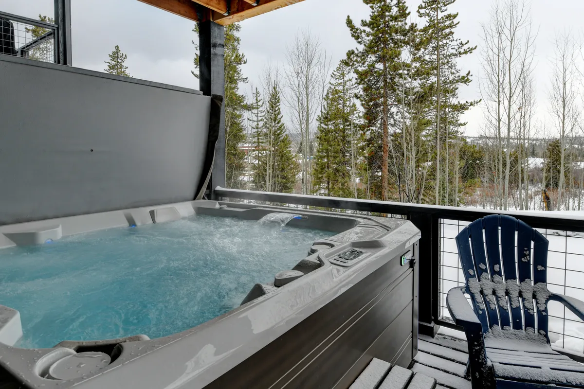 A tranquil, snow-covered deck with a private hot tub surrounded by trees. The setting is designed for soaking in the hot tub while gazing at the winter scenery, with the promise of stargazing and enjoying hot beverages outdoors after a day of adventure.